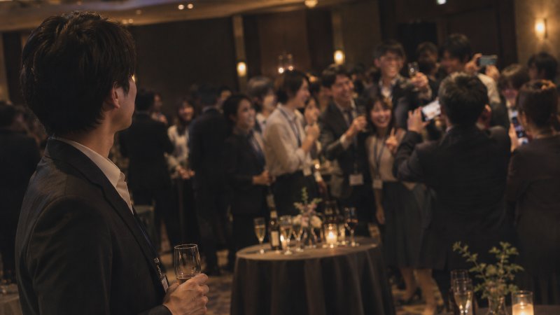 交流会の会場を見ている幹事。奥では参加者が写真を撮り合っている