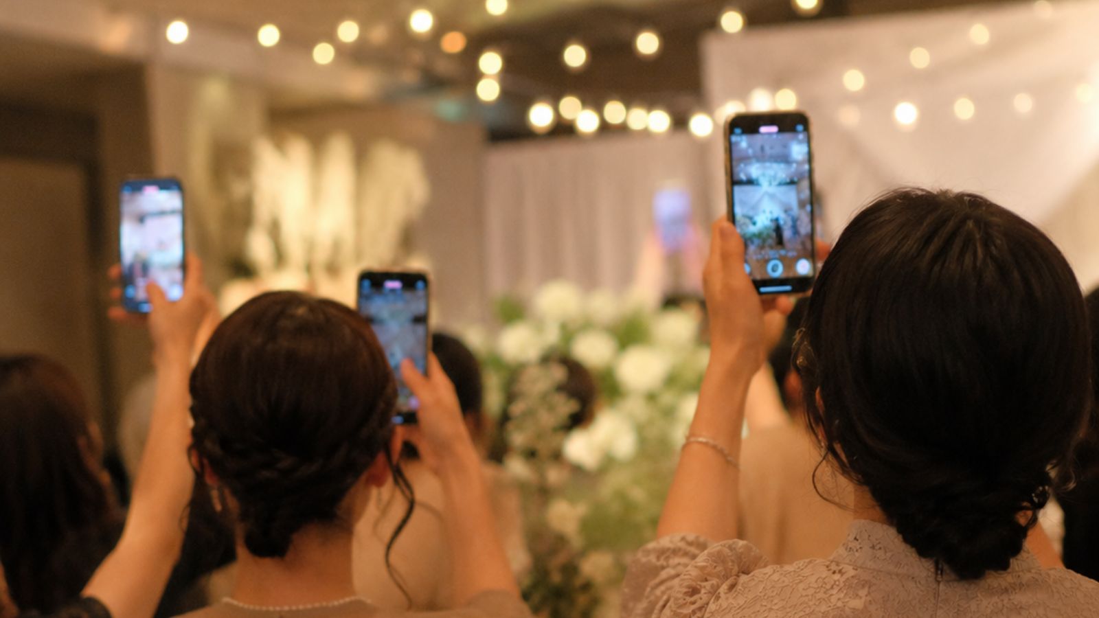 披露宴の会場で、ゲストが何人もスマートフォンをかかげて写真を撮っている様子